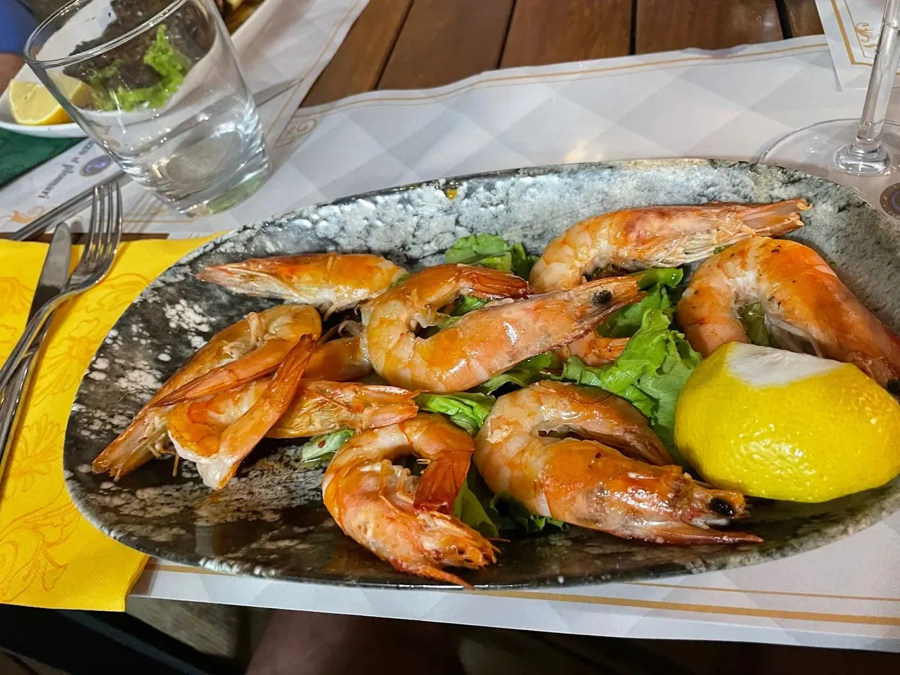 Whole cooked prawns on lettuce leaves on a speckled grey oval platter, with half a lemon