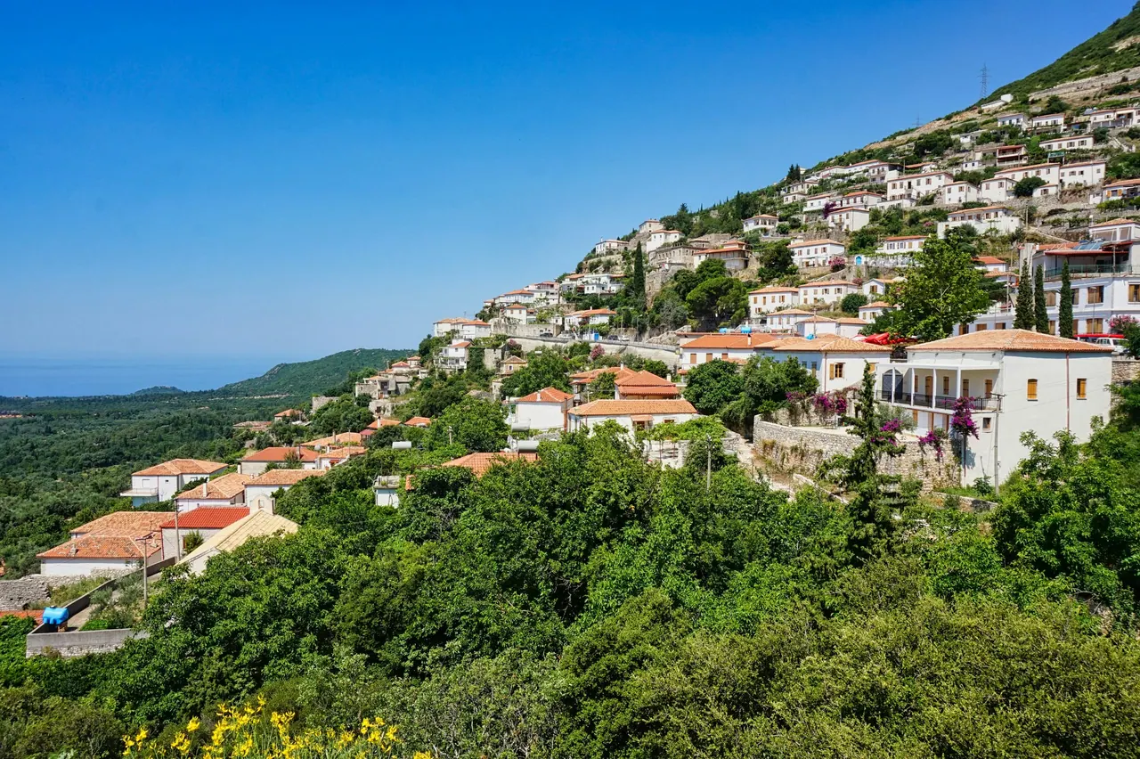 White-rendered houses with terracotta pantile roofs terraced up a hillside above the coast at Qeparo