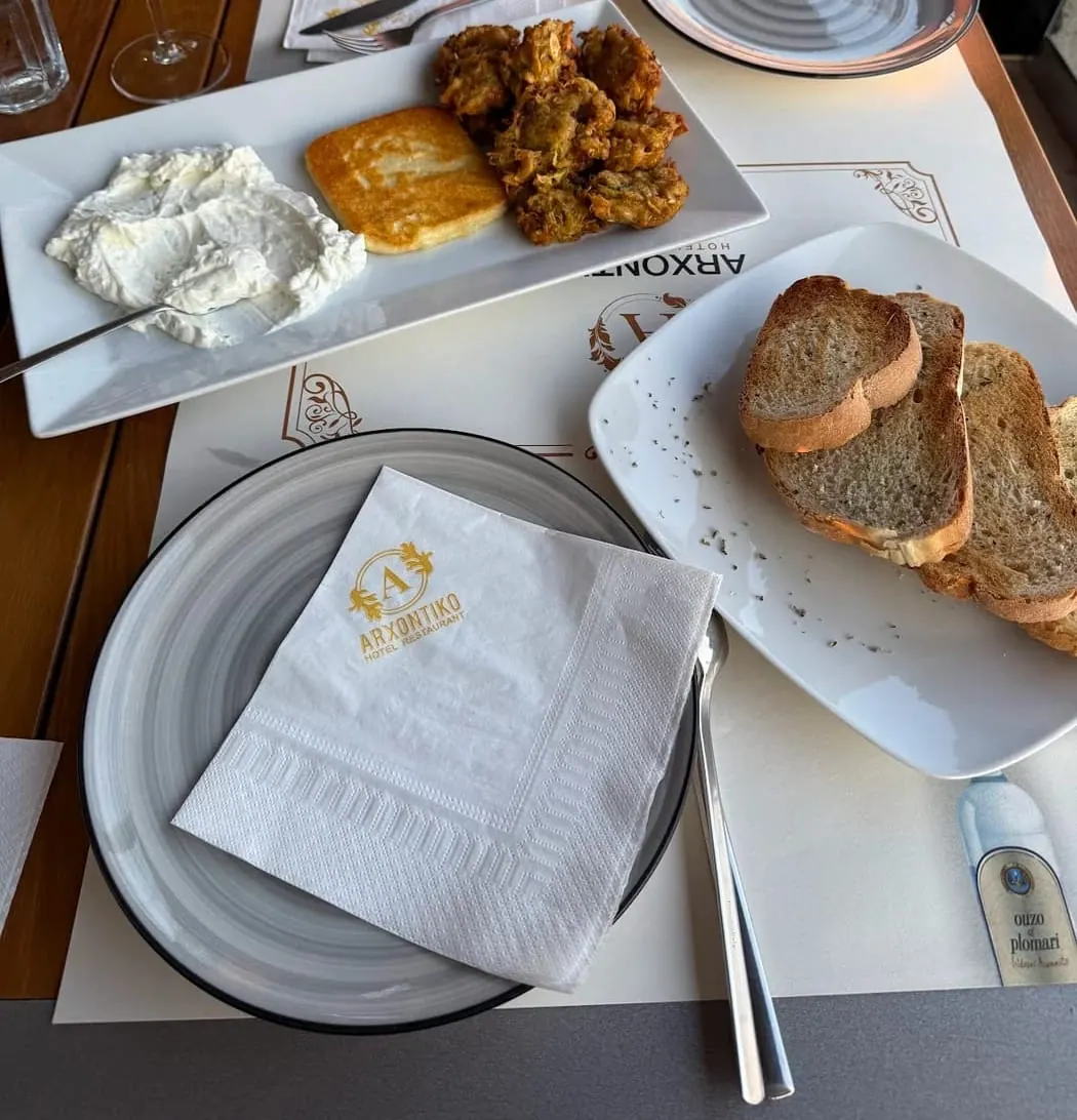 A plate of thick yoghurt, a square of fried cheese and courgette fritters beside toasted bread, on a table set with an Arxontiko monogrammed napkin