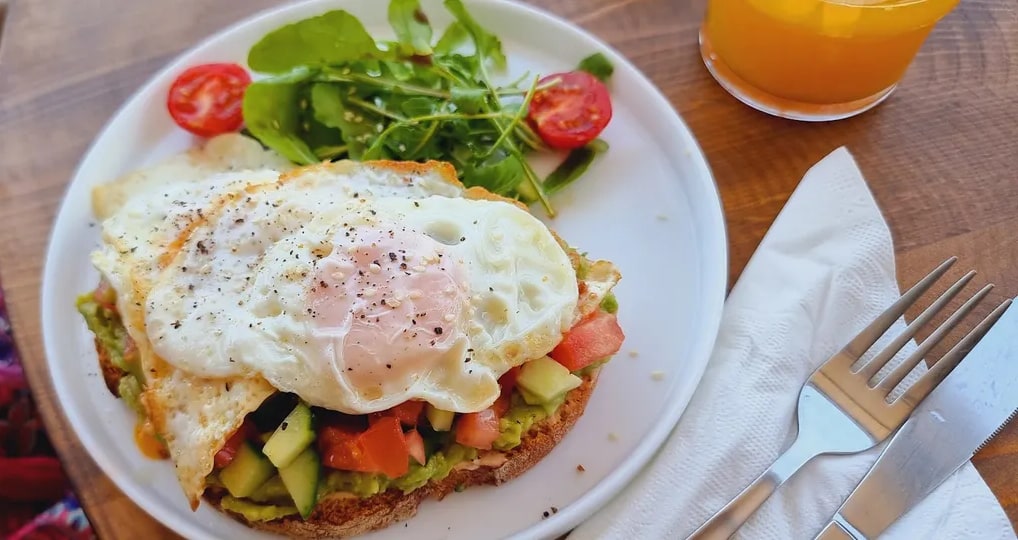 Avocado on toasted sourdough under two fried eggs, with rocket and a glass of orange juice