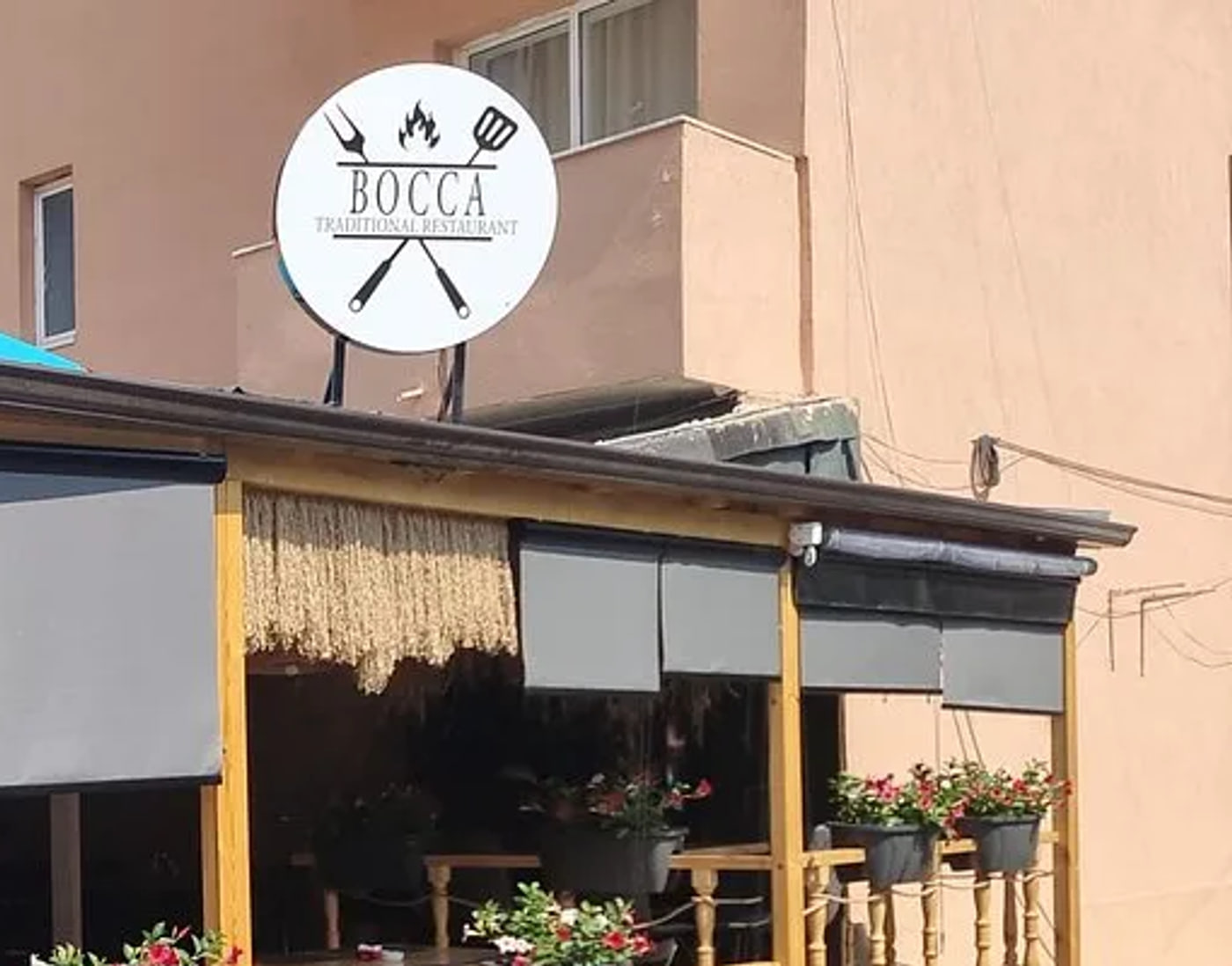 The round white BOCCA sign standing above the veranda roof, lettered TRADITIONAL RESTAURANT beneath a flame and a crossed grill fork and spatula