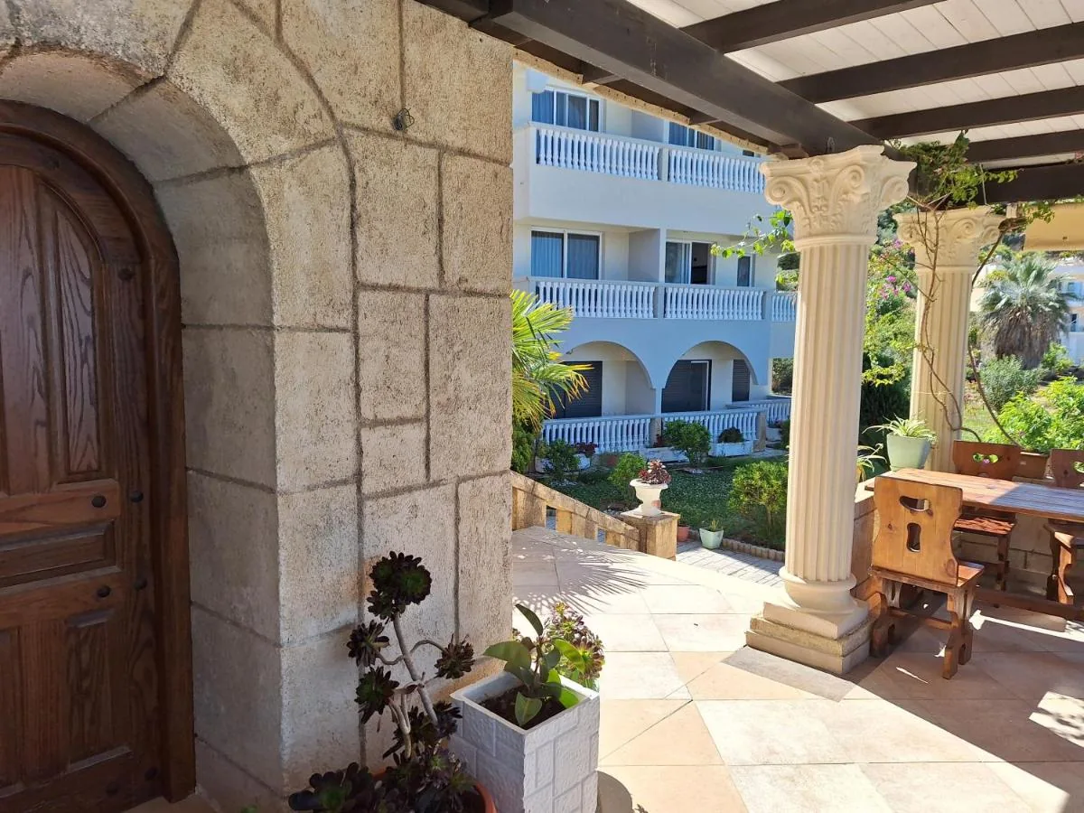 A rusticated limestone arch with a studded oak door at Castle Hotel, a fluted column carrying a timber pergola, and the balustraded guest block behind