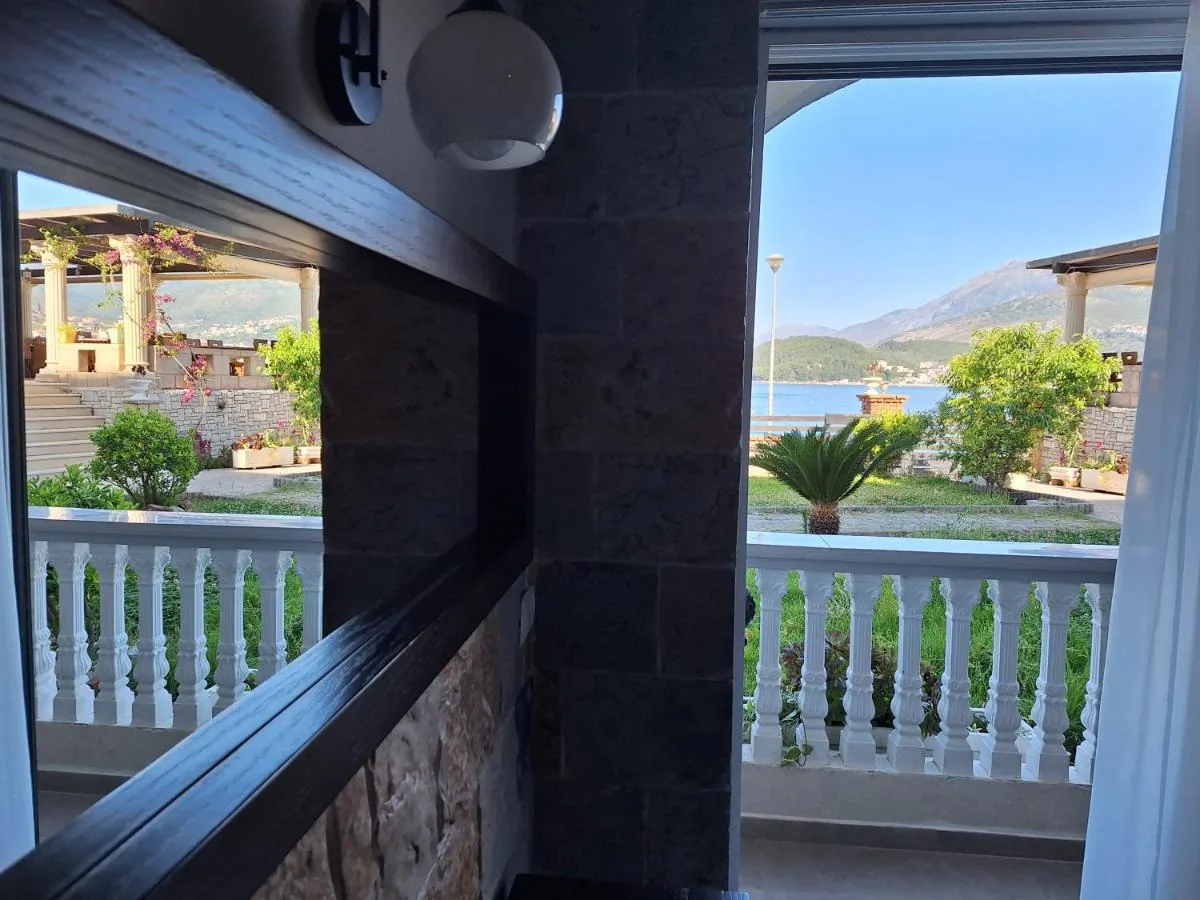 A stone-framed slot cut through a wall at Castle Hotel, the pergola and garden through it, and beside it an open doorway onto a balustraded balcony with a sago palm, the sea and the headland