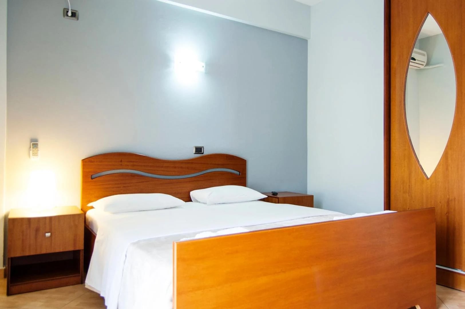 A double bed with a curved cherry-wood headboard in a pale blue-grey room