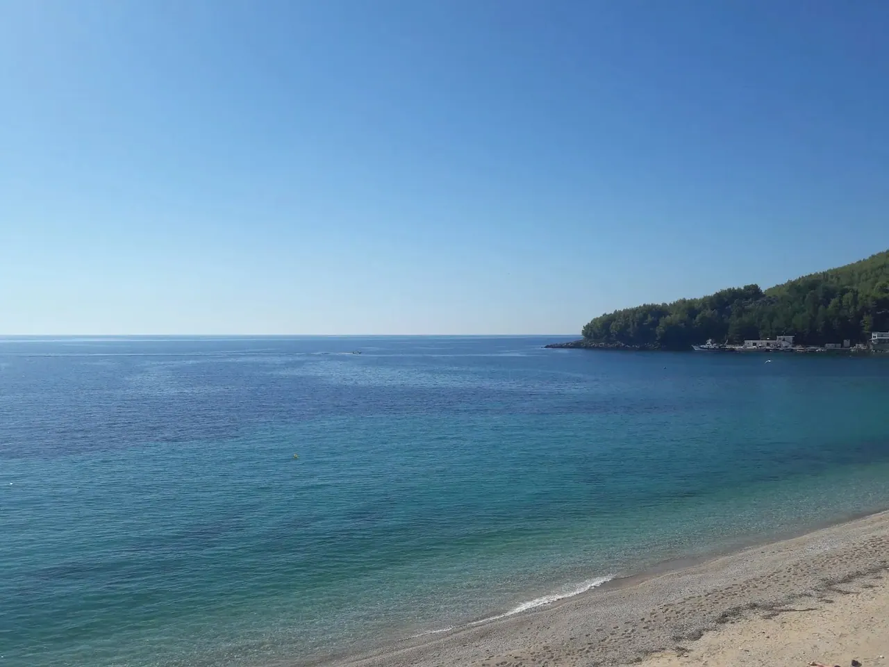 A quiet turquoise cove closed off by a wooded headland, seen through the shape of the hotel's D monogram