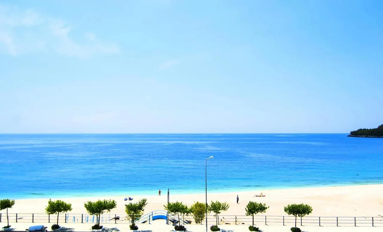 The beach and the coast road seen from an upper balcony, with clear blue water
