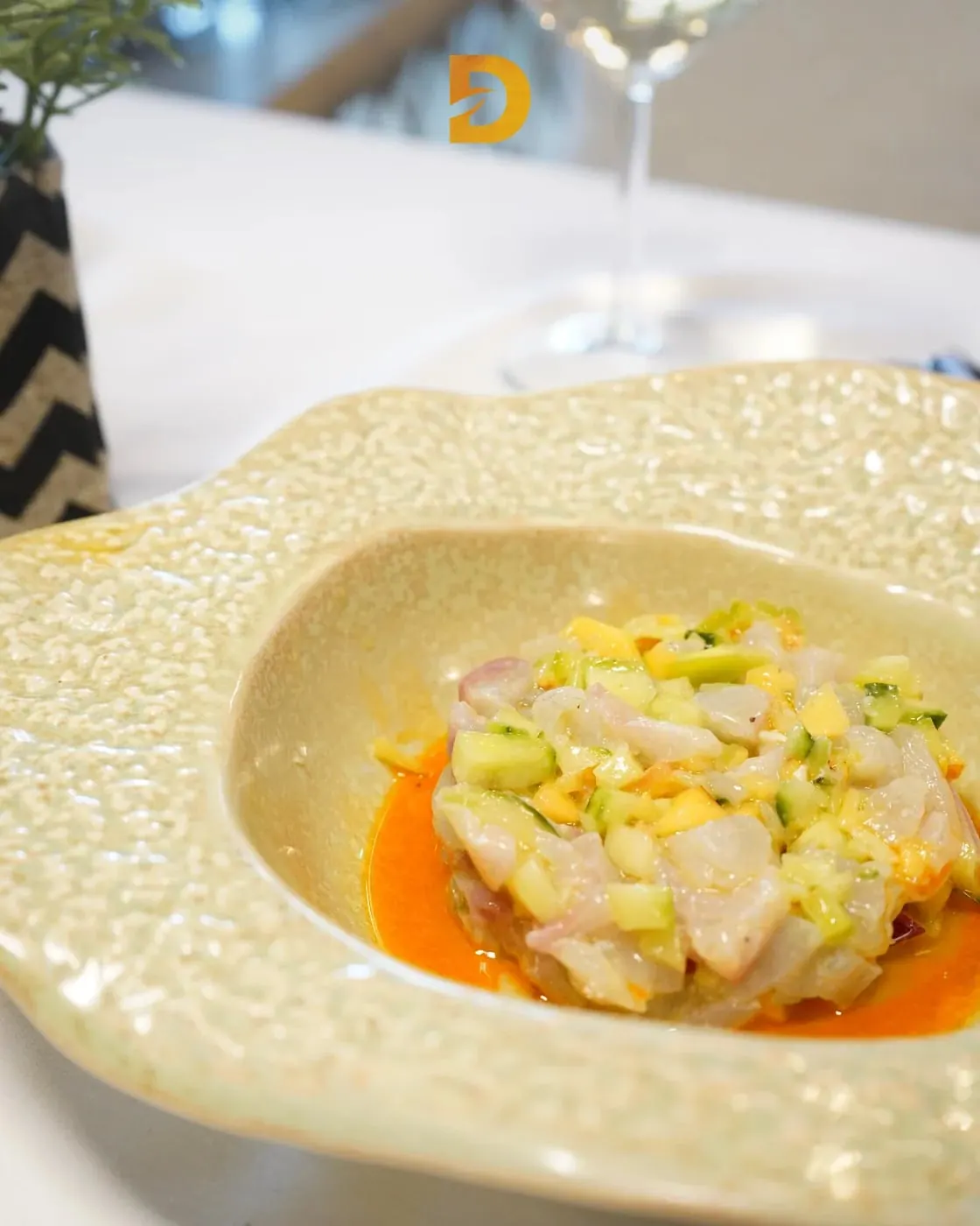 Diced raw white fish dressed in citrus, ringed by orange pepper oil in a pale bowl