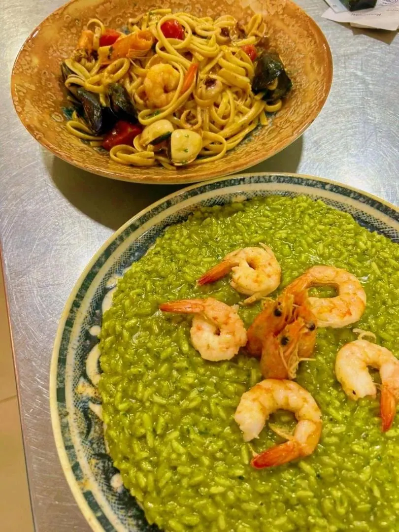 A bright green herb risotto with prawns laid over it in a patterned bowl