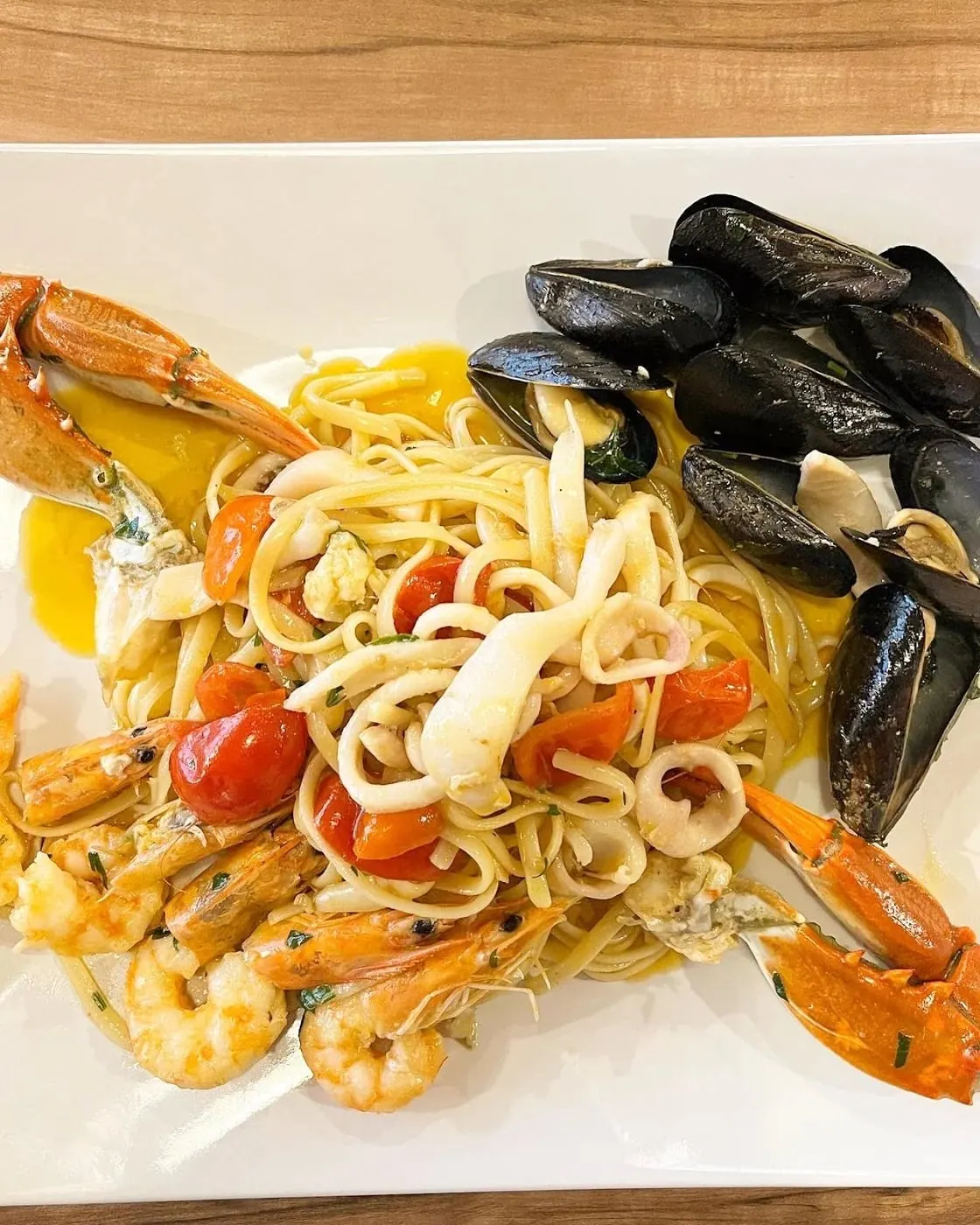 Ribbon pasta tangled with mussels, squid rings, whole prawns and two crab claws on a white plate