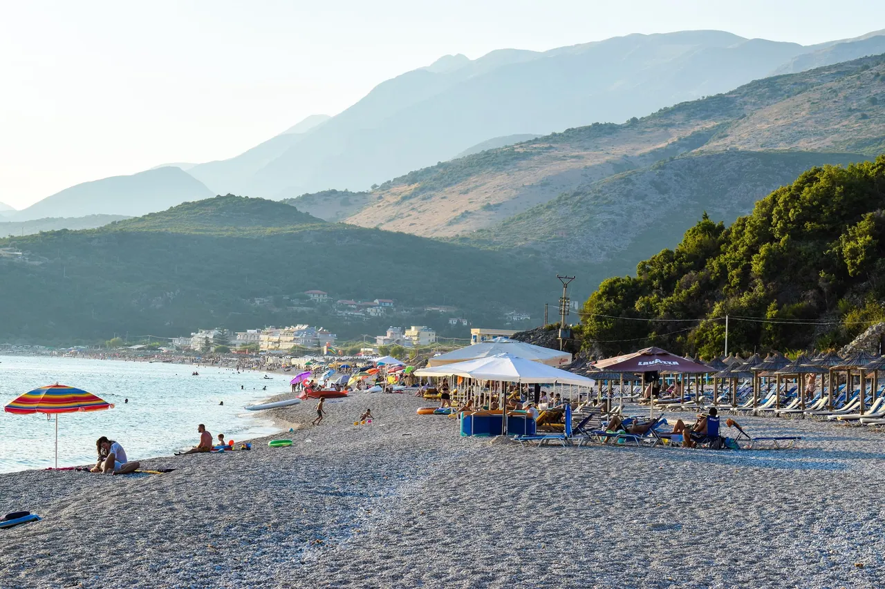 Sunbeds and swimmers along the wide shingle sweep of Livadhi beach below green hills