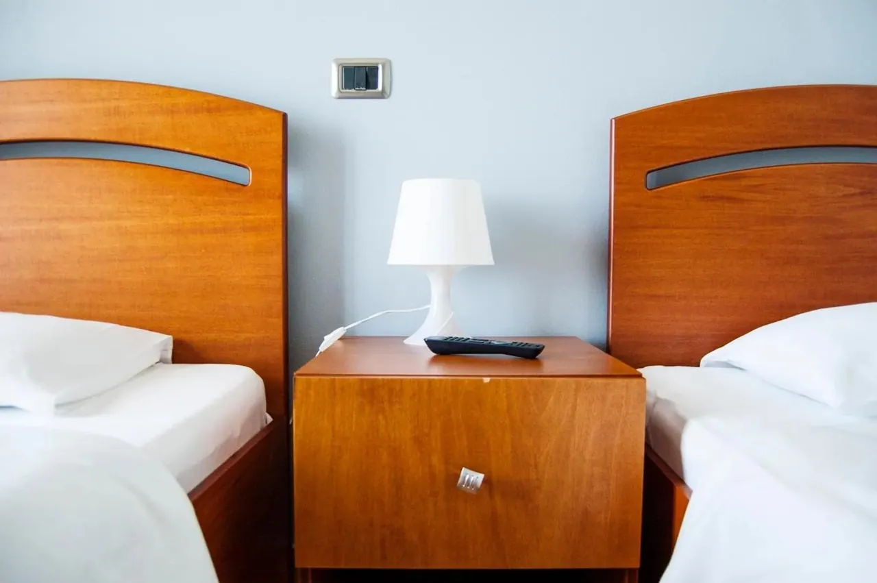 Two single beds either side of a cherry-wood cabinet with a lamp and a remote