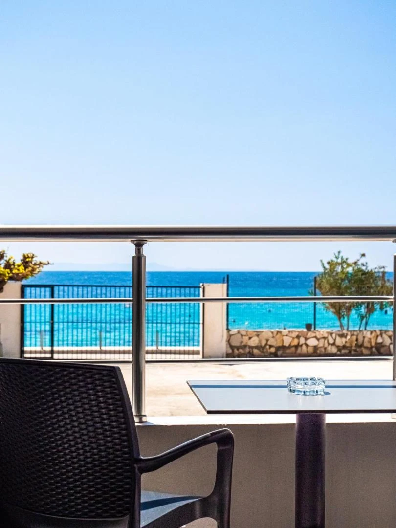 Balcony table above the turquoise shallows, with the property's own forecourt and its sea wall directly below