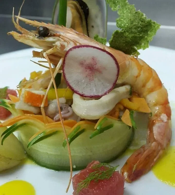 A plate out of the Enigma kitchen: a whole prawn over squid and mussel in a nest of ribboned carrot, with radish and pink grapefruit cut thin and a yellow oil pooled on the plate