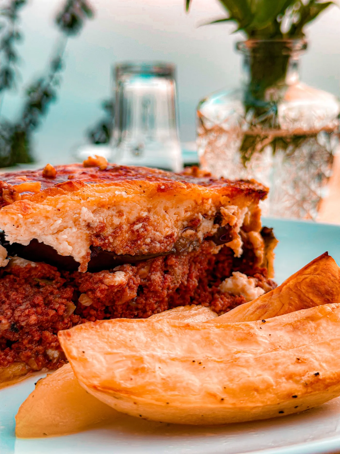Slice of moussaka with browned béchamel and roast potato wedges at Fig & Olive, Himarë