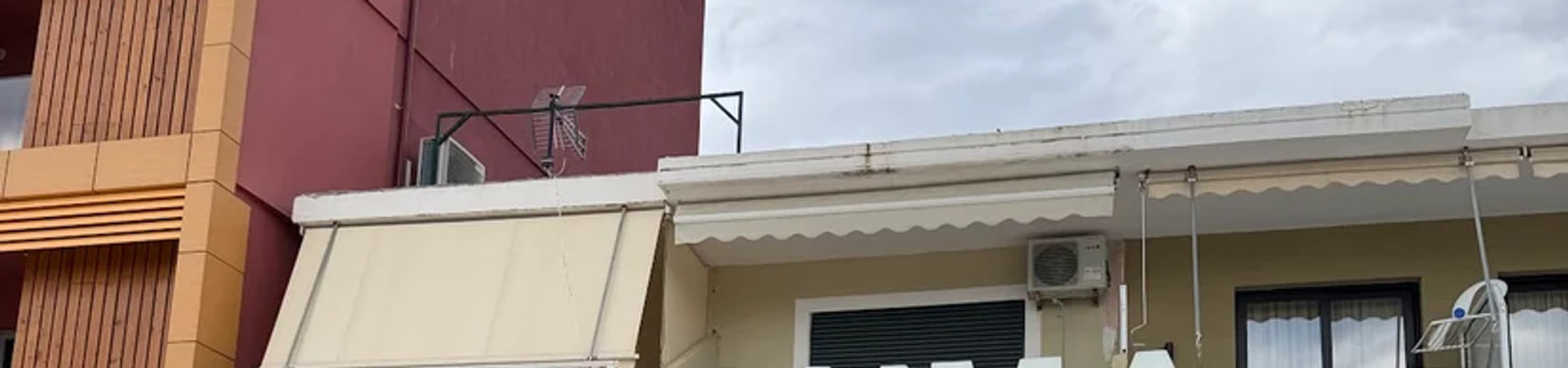 The soffit and scalloped canvas awning above the restaurant front, the maroon flank of the neighbouring block rising behind it under an overcast sky