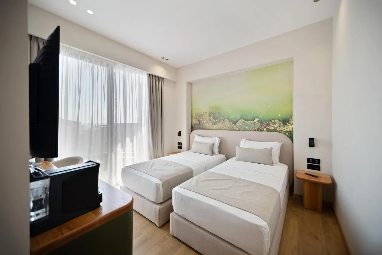 A twin room at Hotel Potami with two beds against a painted green panel, a wall-mounted television and floor-to-ceiling curtains