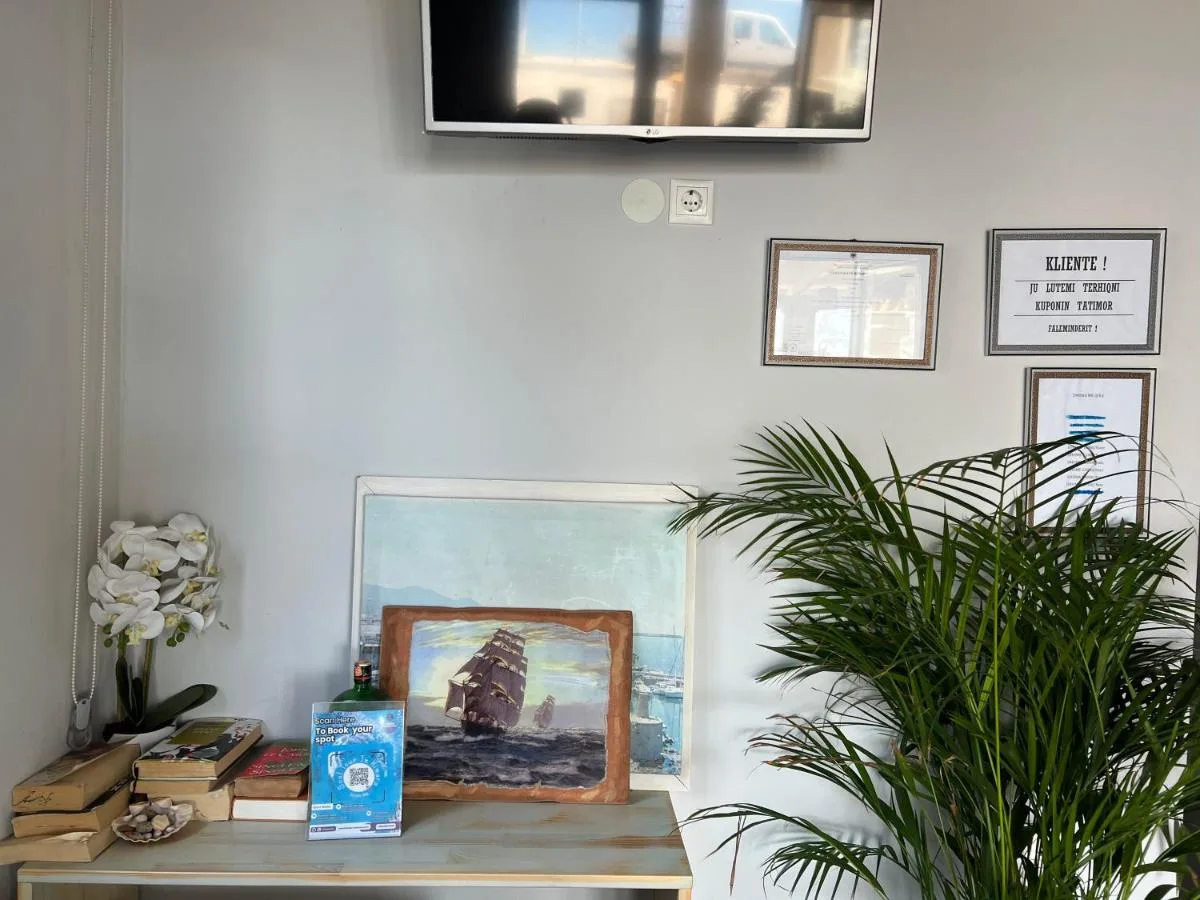 The reception counter at Hotel Prinos with a framed painting of a tall ship standing on it, a stack of old books, an orchid and a palm