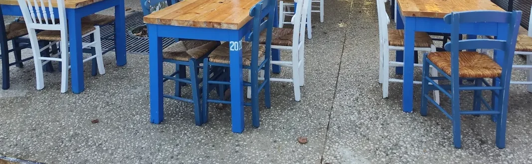 Cobalt-blue tables with bare wood tops, and white and blue rush-seat chairs, on the pebble-wash concrete of the terrace