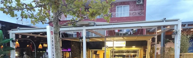 The street front of I Love Souvlaki in Spile, its white pylon sign under a plane tree