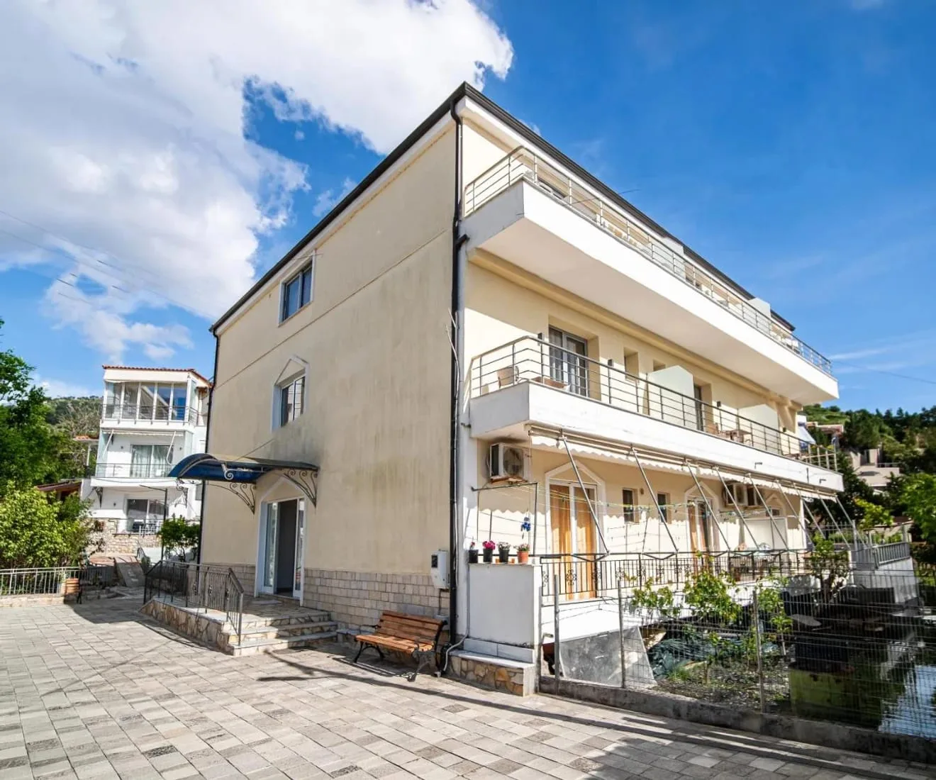 Exterior of Vourtaréa Guesthouse in Potam, Himara, with balconied rooms above a paved forecourt