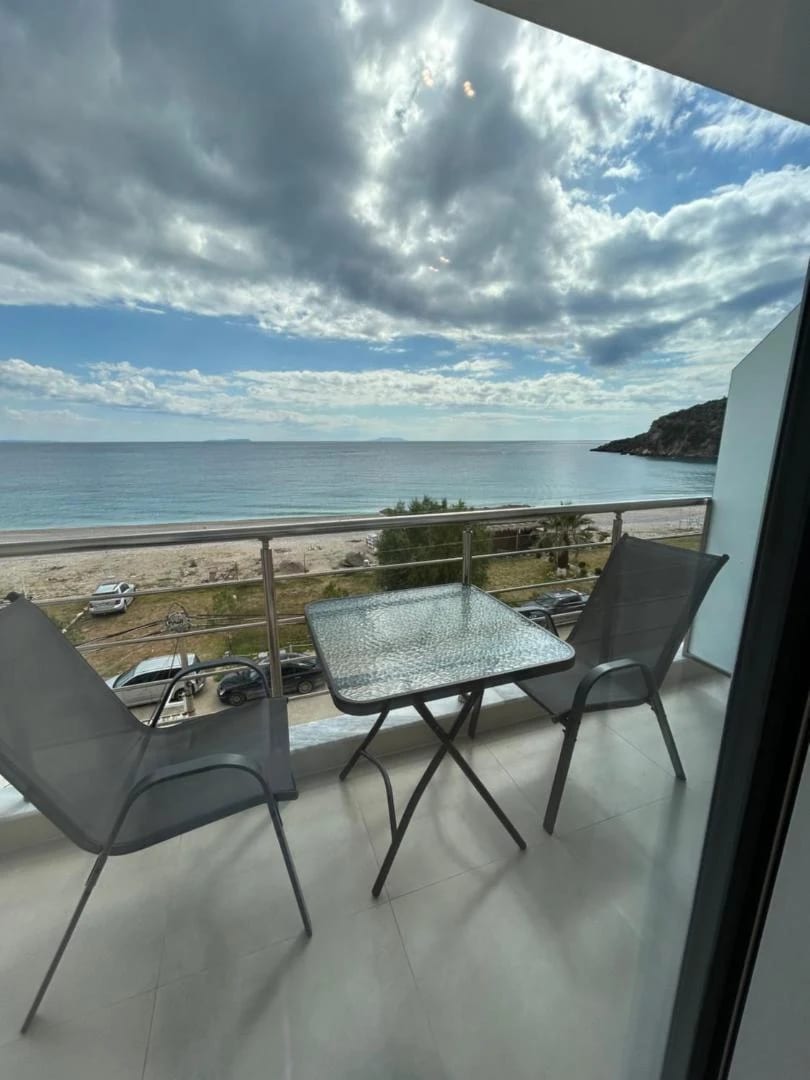A balcony table and chairs at Ionian View, looking across the beach road to Livadhi bay curving away towards the headland