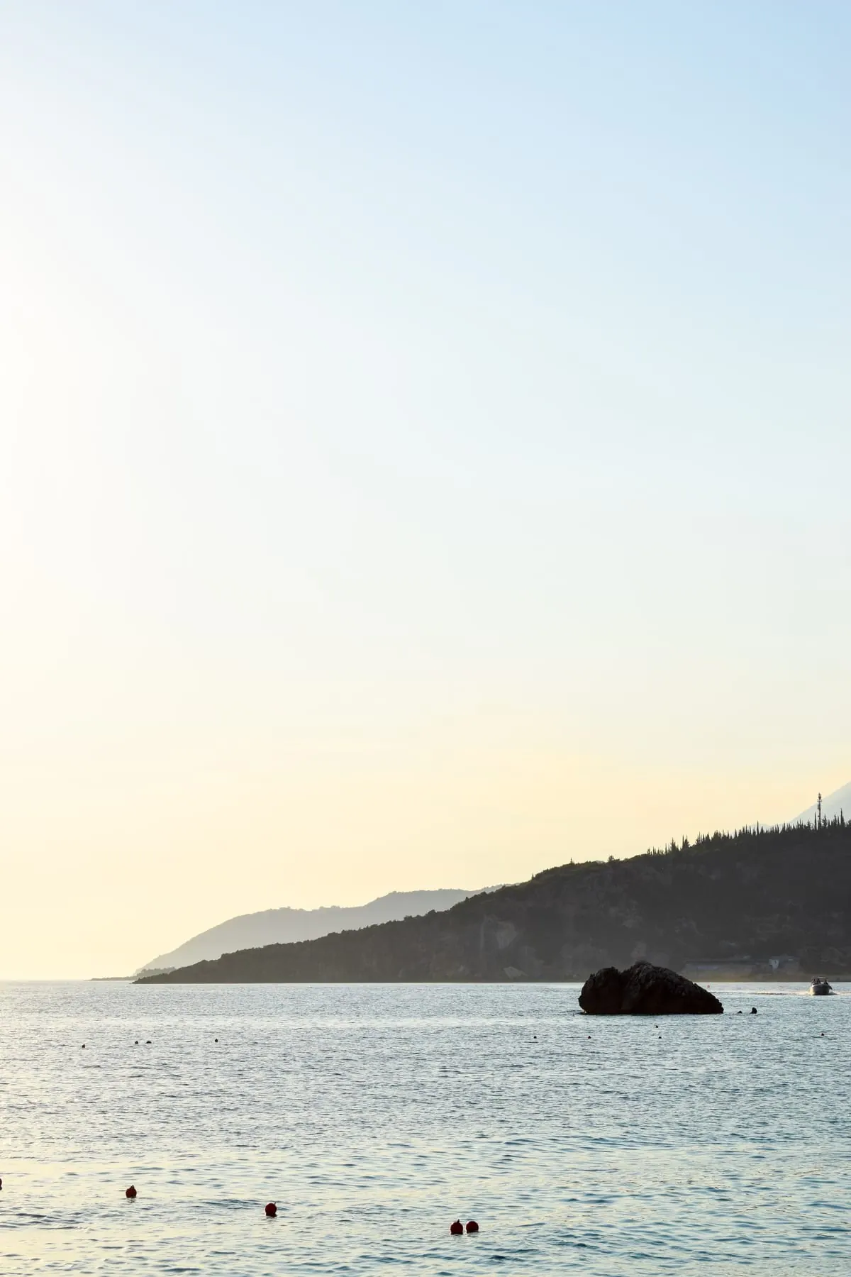 Livadhi bay at golden hour, a rock standing out of the calm water below a wooded headland