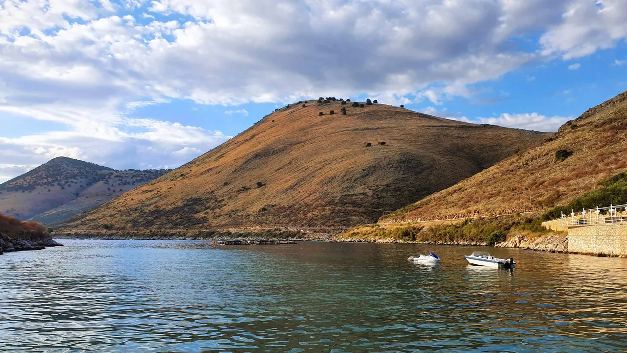 The near-enclosed bay at Porto Palermo, a bare headland above the water and a stone promenade along the shore