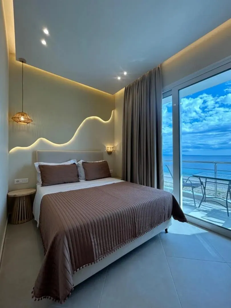 A deluxe double room, its headboard lit by a wave of concealed light, the balcony door opening onto the Ionian