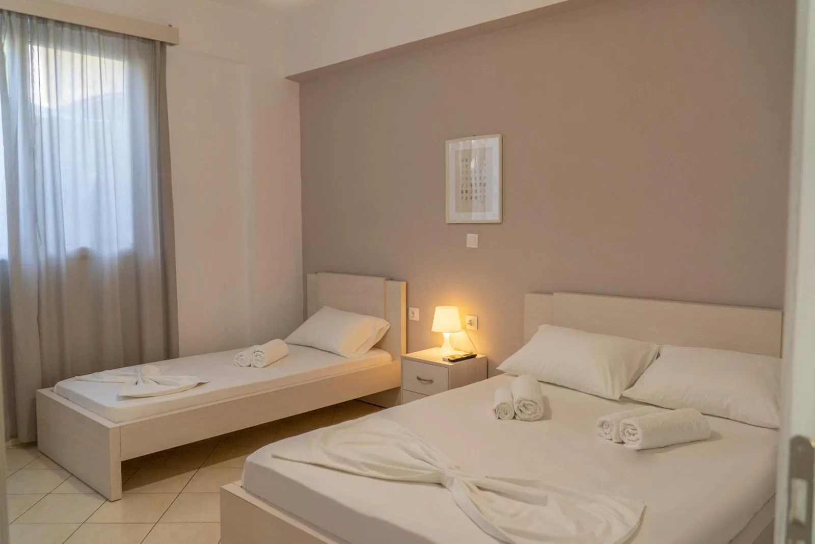 A room made up with a double bed and a single bed, towels folded on both