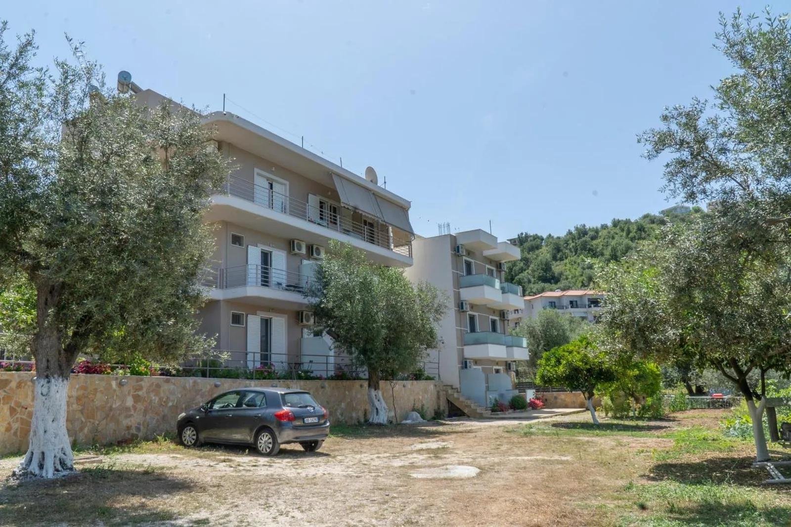 The guesthouse seen from the olive-shaded parking, behind a flagstone wall