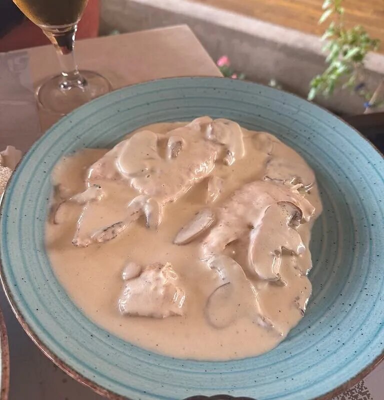 Escalopes under a cream and mushroom sauce, on the same pale blue plate, with a glass of white beside it.