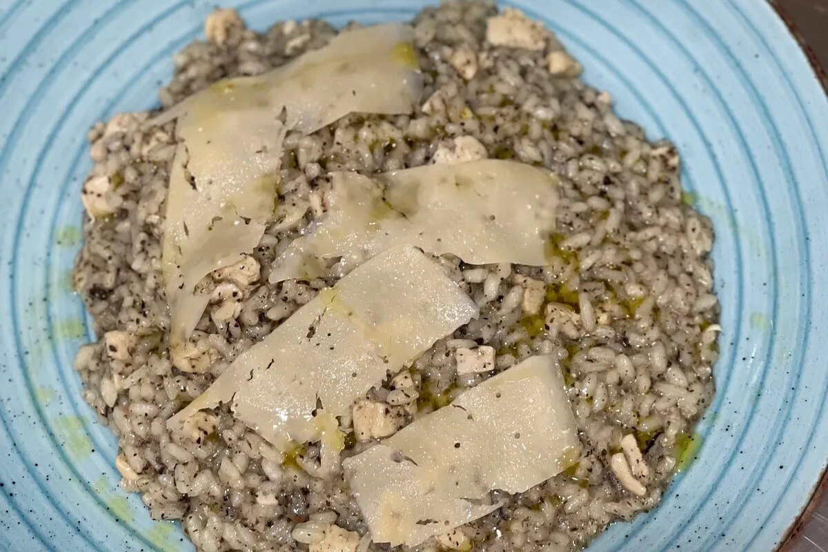 A rice dish finished with shaved hard cheese and olive oil, on the kitchen's pale blue plate.