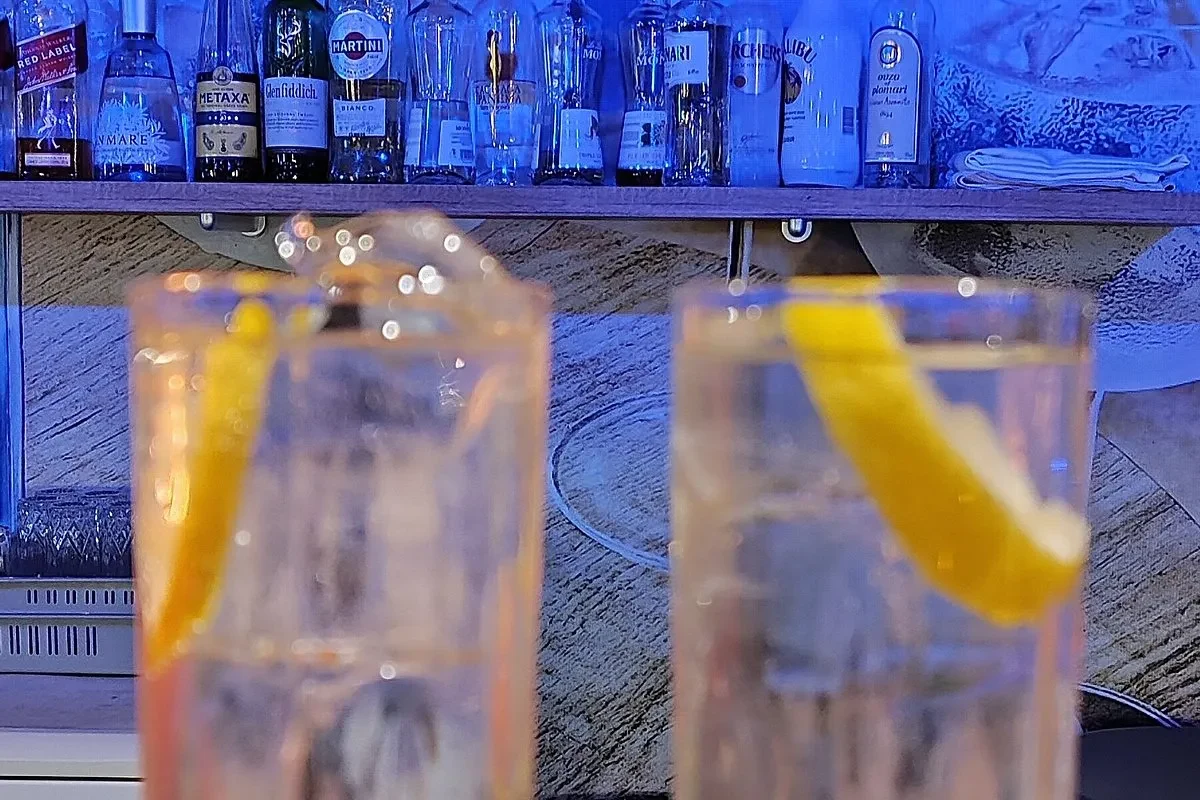 A back bar shelf of spirits under blue light, with two tall drinks and curls of citrus peel standing in front of it