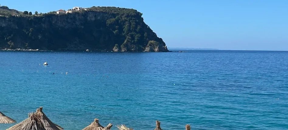 The wooded promontory that closes the south side of the bay at Namos Beach, with a small boat moored on flat turquoise water