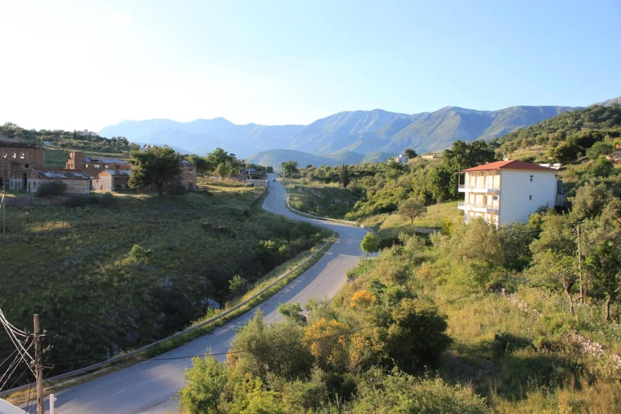 The SH8 curving down between green slopes, a derelict brick complex on the left and the mountain ridge along the horizon