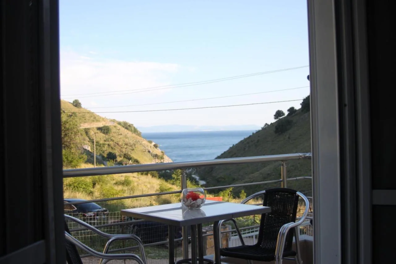The Ionian seen from a balcony as a wedge of blue water between two green hillsides, with a table and chairs in the foreground