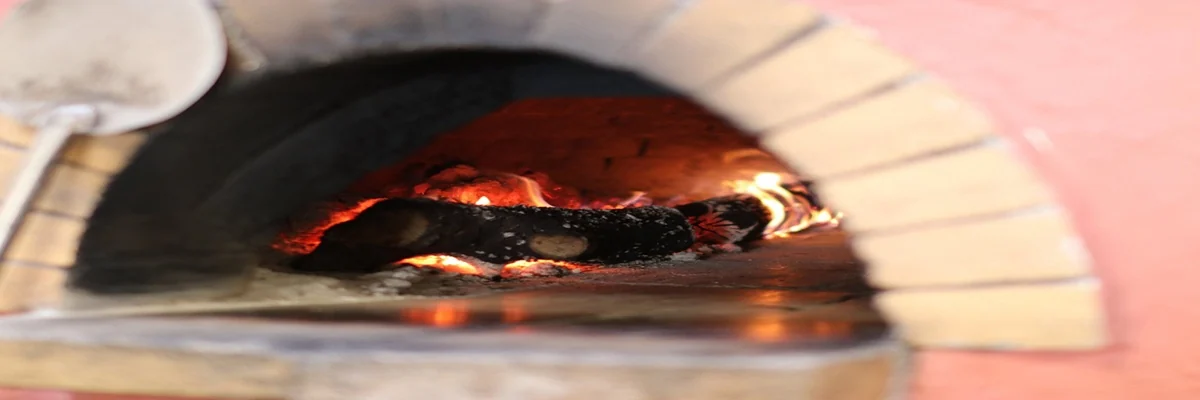 The mouth of the wood-fired oven, cream firebrick arch set in terracotta render, fire inside