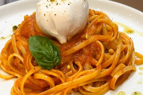 Ribbon pasta in tomato sauce with a ball of soft white cheese and a basil leaf