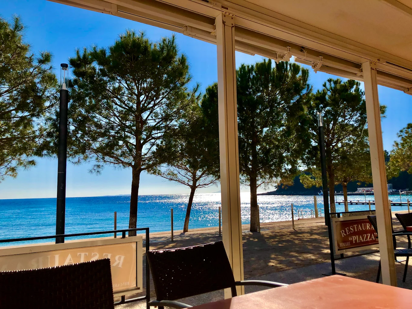 Looking out from the terrace of Piazza through the awning posts to the pines, the promenade and the bay