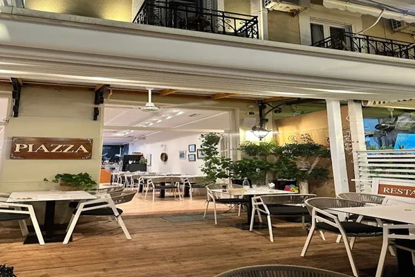 A timber PIAZZA board lit on the wall of the covered terrace, tables and plants under lamplight