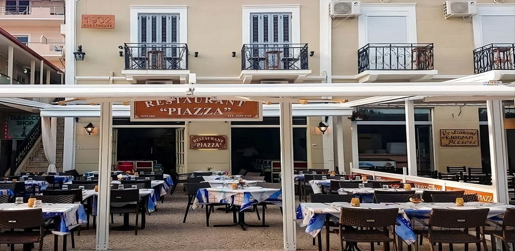 The frontage of Restaurant Piazza in Himarë, the terracotta sign hanging under the white awning above laid tables