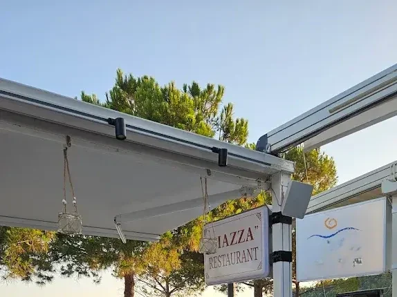 The Piazza sign at the edge of the terrace awning, pines and open sky behind it