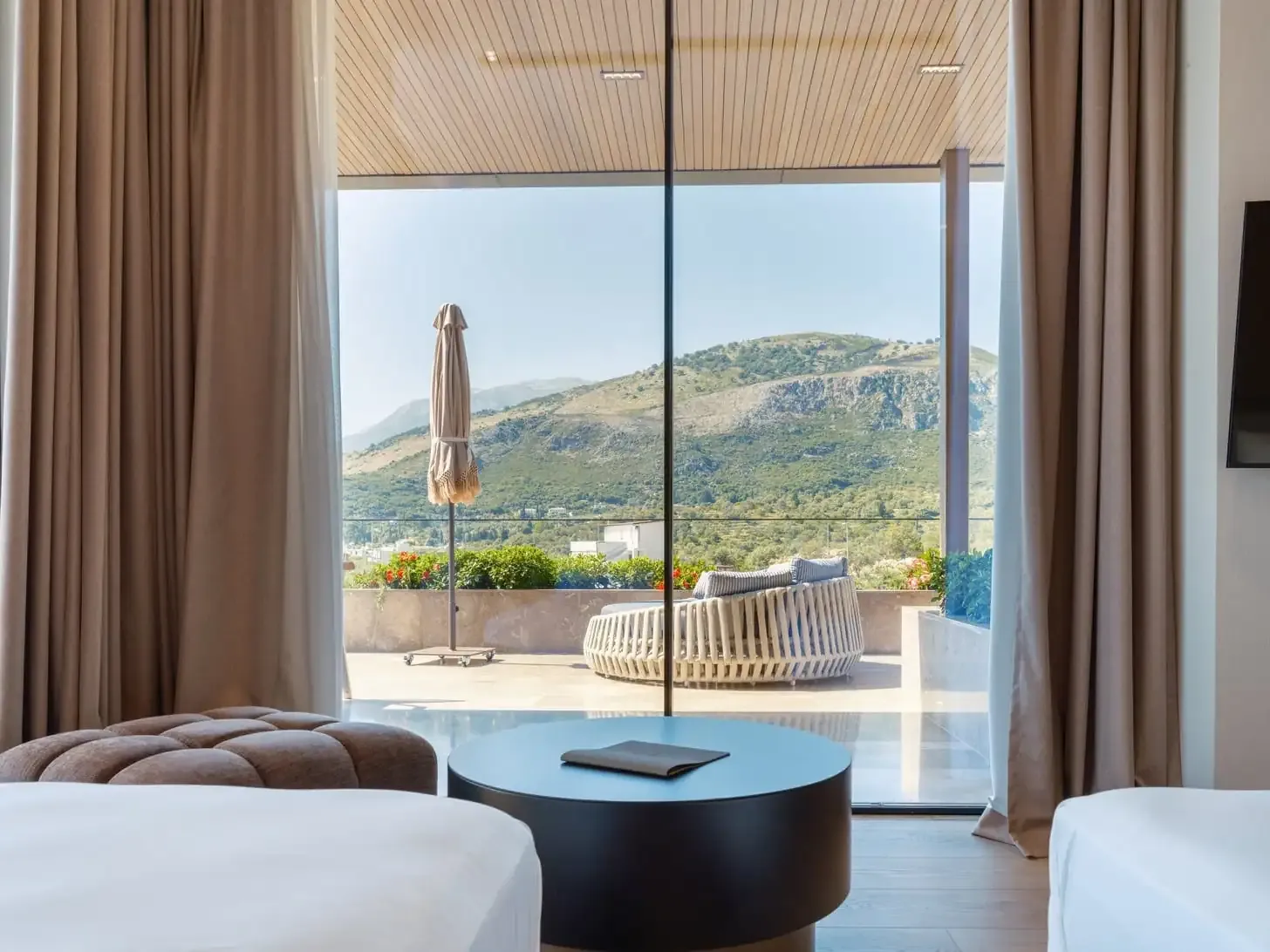 The oversized furnished balcony of the Deluxe Suite at Prado seen from inside, a rattan daybed and a folded parasol against the green ridge