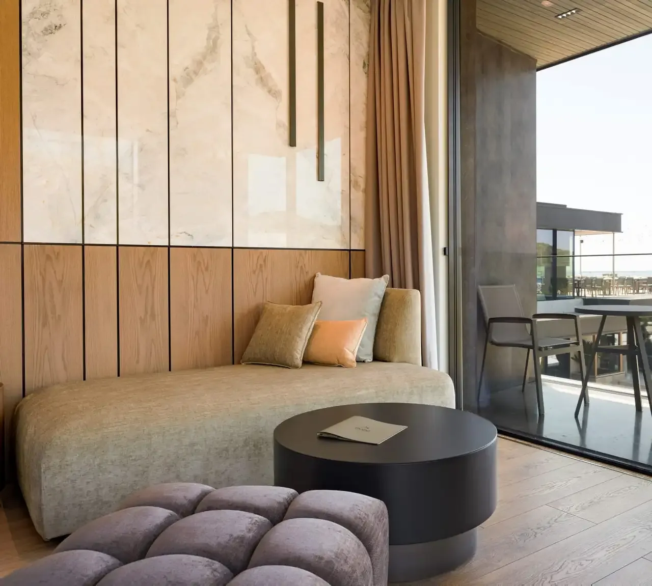 The living area of a sea-view Junior Suite, a long sofa and a low table against marble and oak, the terrace through the glass