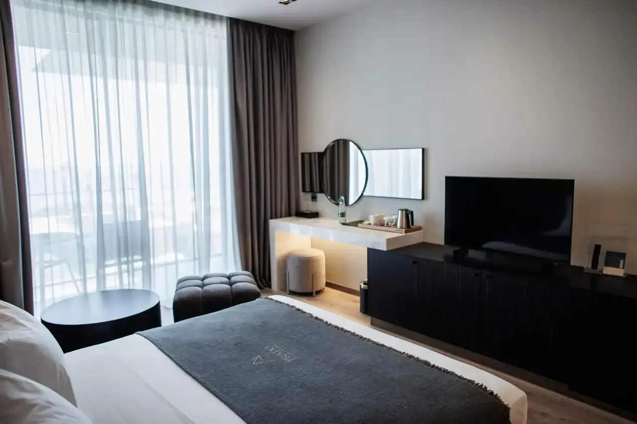 A Standard Room with Sea View: the bed facing a desk, mirror and television, daylight coming in from the balcony