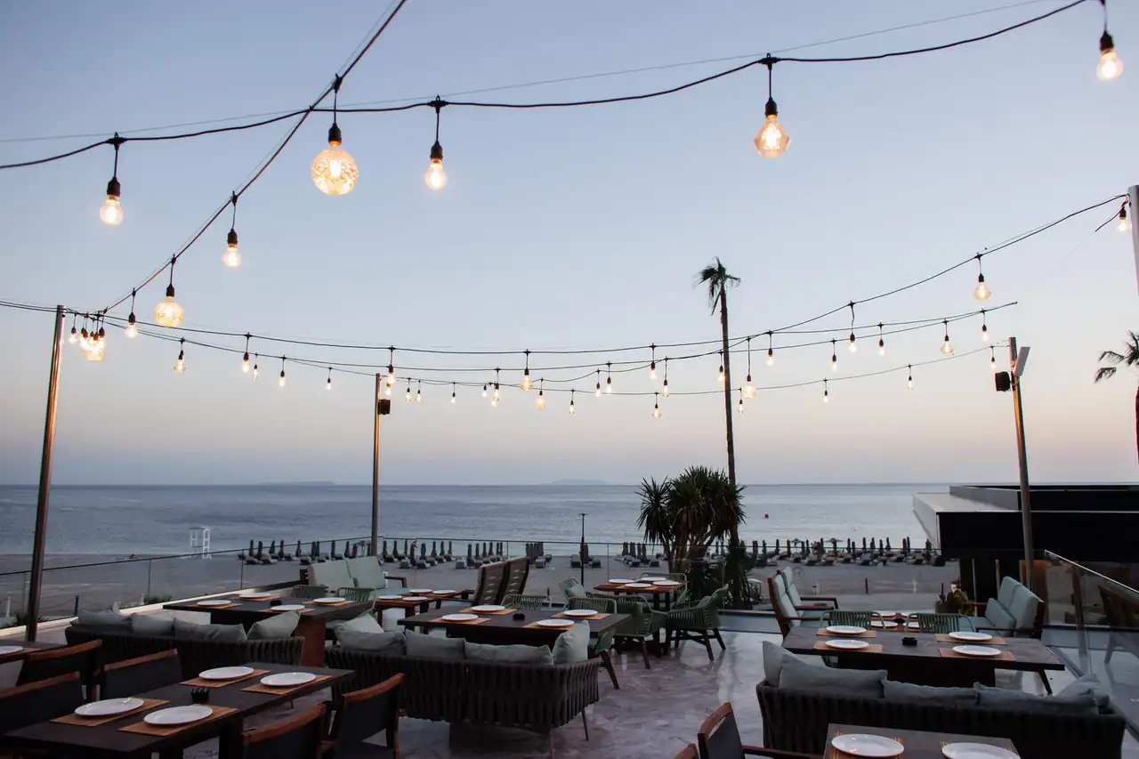 The sushi bar terrace at dusk, festoon lights strung above laid tables and the beach beyond