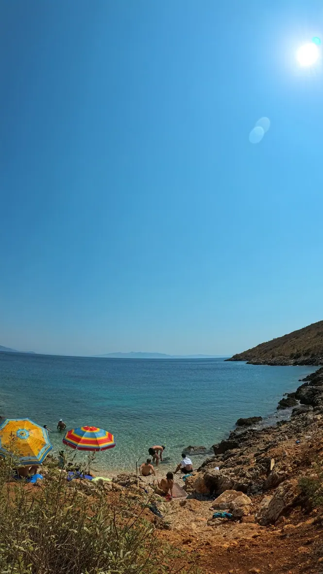 Busy beach club bay on the Himara Riviera with umbrellas and turquoise water where watersports are rented