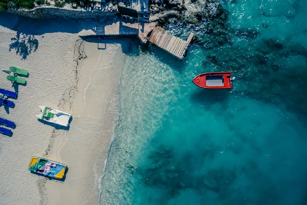 Quiet Ksamil cove — pedalboats on white sand and a red speedboat moored in turquoise water