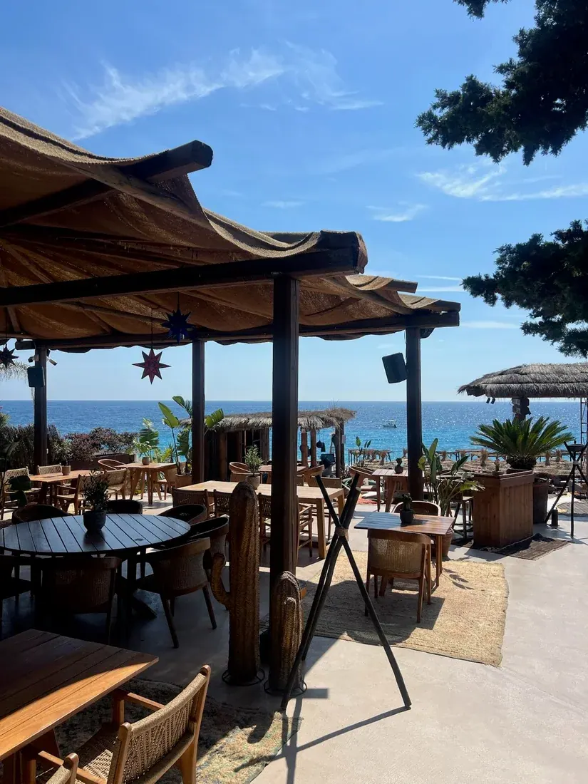 Moyo Drymades beach club terrace with thatched umbrellas and wooden tables overlooking the Ionian Sea at Drymades