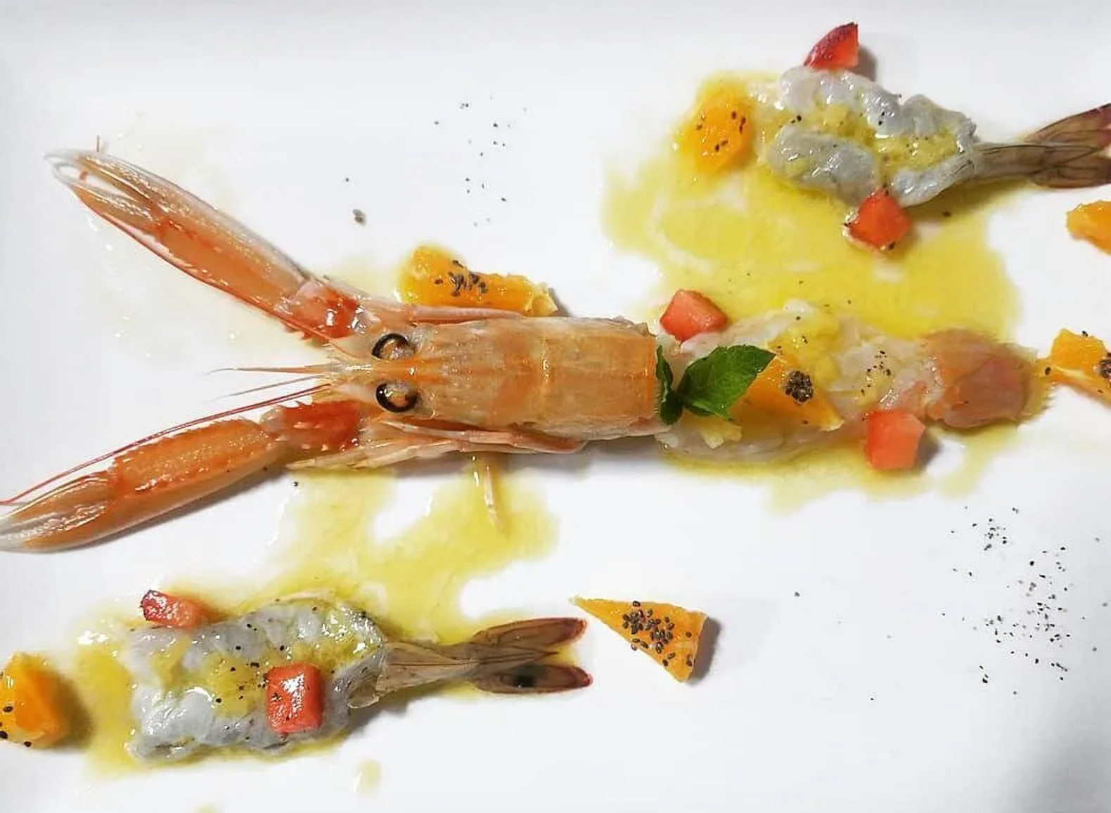 A langoustine served raw on a white plate with citrus, tomato, mint and cracked pepper